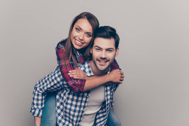 Portrait of his he her she two nice lovely attractive cheerful people married spouses husband wife wearing checked shirt piggybacking having fun isolated over gray pastel background