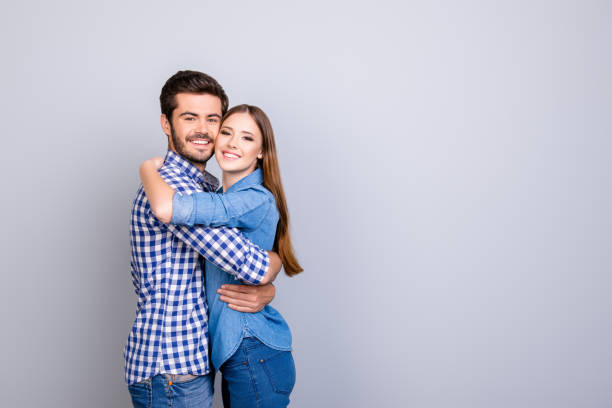 True love, trust, friendship, happiness. Two young cute lovers are looking at the camera and smile, wearing casual outfits, hugging gently on the pure background near copy space